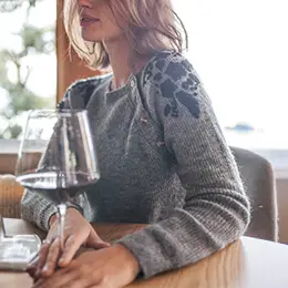 Woman sitting at table with a glass of wine wearing Amberley Dress.